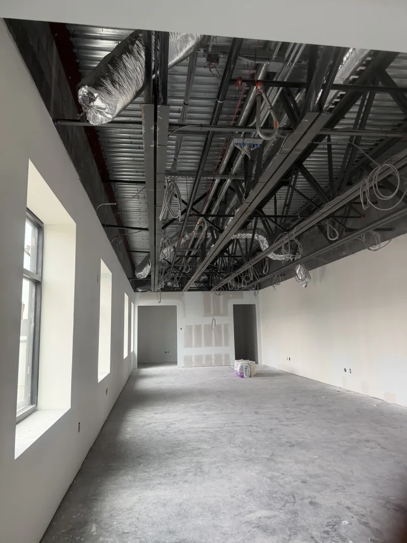 Interior shell painted white, with an exposed black ceiling deck and ductwork above a bare concrete floor