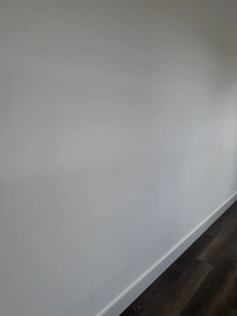 Close-up of a smoothly finished white wall meeting a painted baseboard